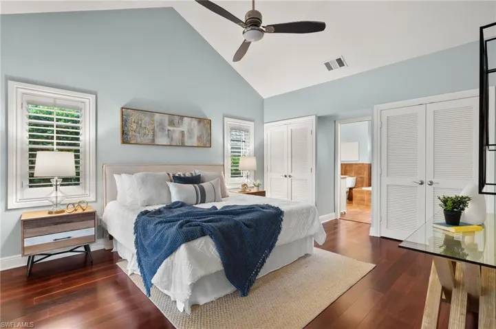 Bedroom with high vaulted ceiling, visible vents, two closets, baseboards, and dark wood-type flooring