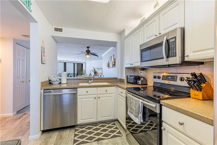 Kitchen with appliances with stainless steel finishes, white cabinetry, light wood-type flooring, ceiling fan, and sink