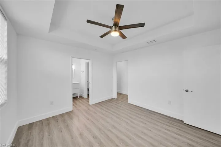 Tray ceiling with integrated ceiling fan, wood-finish flooring, white walls, and bright lighting
