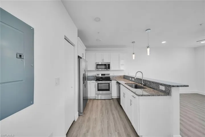 Modern kitchen featuring stainless steel appliances, white cabinetry, a granite countertop, and pendant lighting