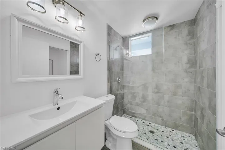 Walk-in shower with gray tile surround, pebble shower floor, and a transom window