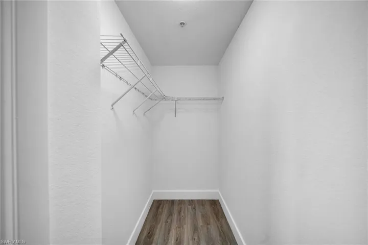 Corner wire shelving system with hanging rod, wood-finish flooring, and white baseboards