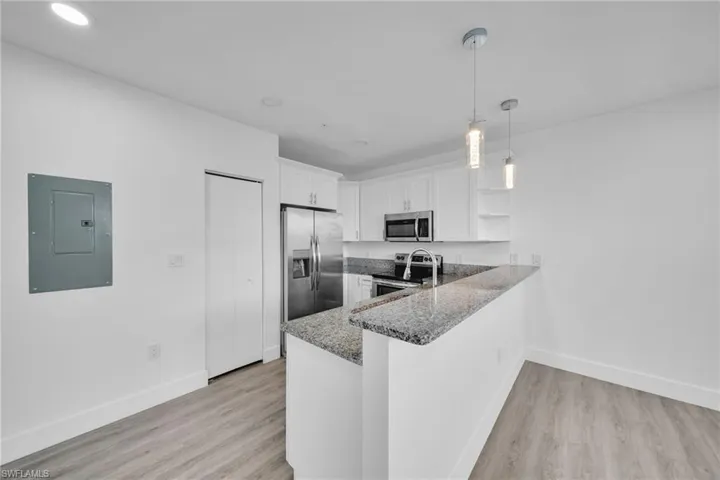 Kitchen featuring granite countertops, stainless steel appliances, white cabinetry, wood-finish flooring, and recessed lighting