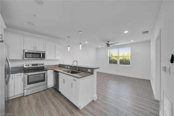 Open-concept living space with wood-finish flooring, white cabinetry, stainless steel appliances, and granite countertops