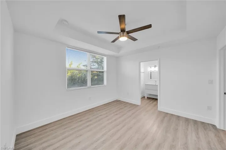Tray ceiling with a modern ceiling fan, wood-finish flooring, and a large window