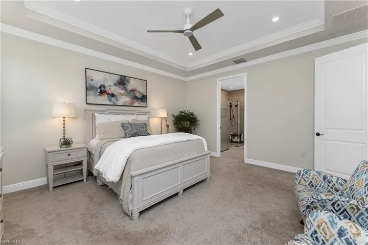 Carpeted bedroom featuring ceiling fan, a raised ceiling, and crown molding