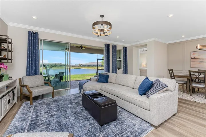 Living room featuring light hardwood / wood-style floors, ceiling fan with notable chandelier, a water view, and ornamental molding
