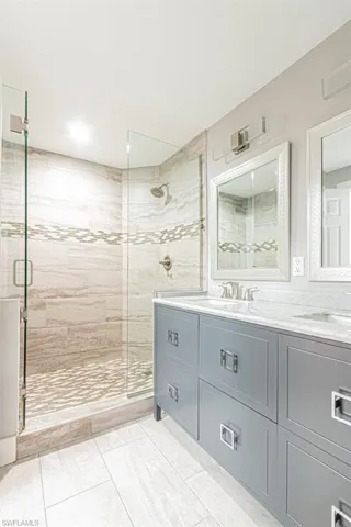 Bathroom featuring double vanity, a shower stall, and light tile patterned floors