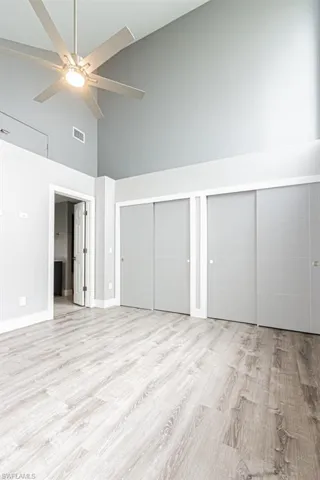 Unfurnished bedroom featuring high vaulted ceiling, two closets, light wood-type flooring, and ceiling fan