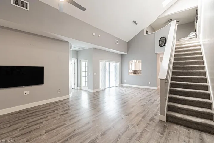 Unfurnished living room with light wood-style flooring, stairs, high vaulted ceiling, and a ceiling fan