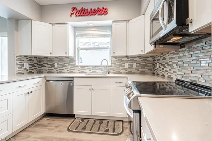 Kitchen featuring appliances with stainless steel finishes, white cabinets, light wood-style floors, and light stone countertops