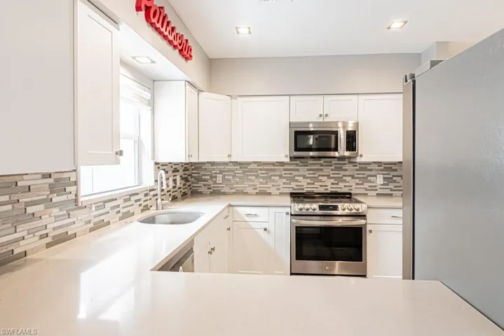 Kitchen featuring appliances with stainless steel finishes, white cabinetry, tasteful backsplash, and light stone counters