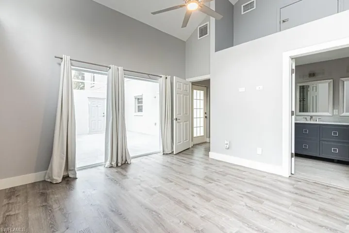 Unfurnished bedroom with light wood-style floors, high vaulted ceiling, ceiling fan, and connected bathroom