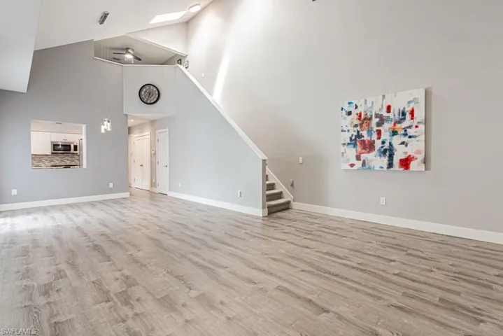 Unfurnished living room featuring light wood-style flooring, high vaulted ceiling, stairs, and a skylight