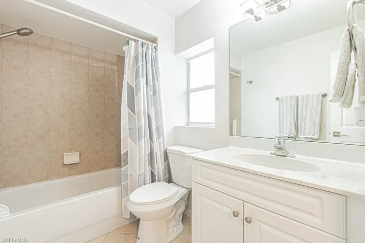 Bathroom with shower / bath combination with curtain, light tile patterned floors, and vanity