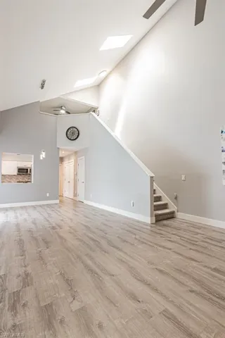 Unfurnished living room featuring a ceiling fan, high vaulted ceiling, light wood finished floors, stairs, and a skylight