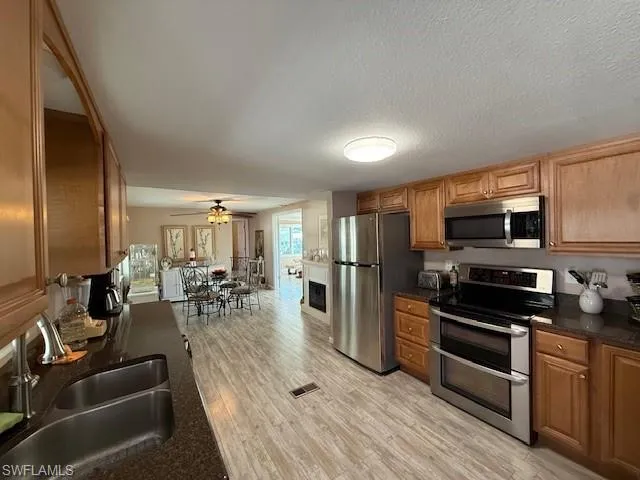 Kitchen with brown cabinetry, dark countertops, appliances with stainless steel finishes, light wood-style floors, and a sink