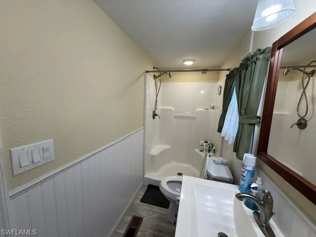 Bathroom with a textured ceiling, a textured wall, a wainscoted wall, a sink, and a shower stall