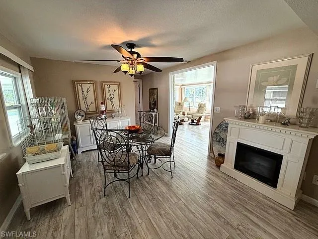 Dining area featuring baseboards, a glass covered fireplace, ceiling fan, wood finished floors, and a textured ceiling