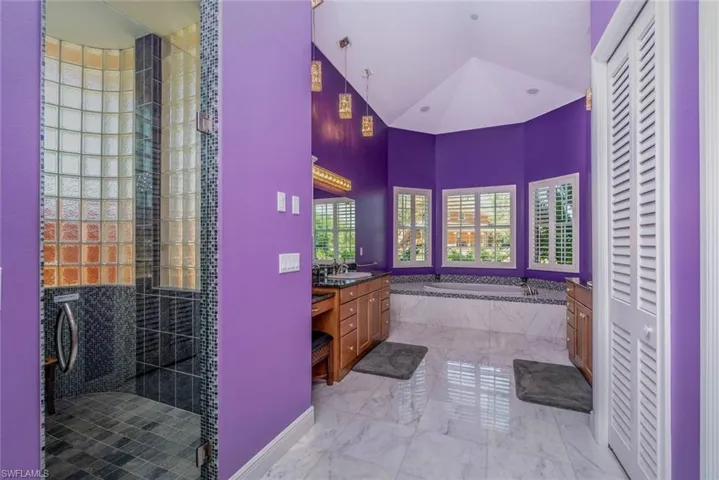 Master Bathroom downstairs with linen closet, dual vanities & sinks, jetted tub, rain shower, private toilet room, marble  flooring, and high vaulted ceiling