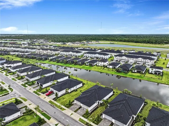 Aerial perspective of a planned community featuring multi-family structures with dark shingle roofing, paved streets, and a canal