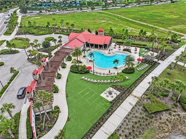 Community amenity center featuring a resort-style pool, expansive stone-paved patio, extensive wood-beam pergola, manicured lawn, and hardscaped fire pit area