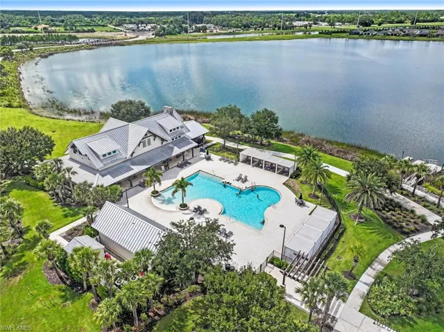 Waterfront amenity center featuring a resort-style swimming pool, expansive paver sun deck, covered cabana structures, and mature palm landscaping