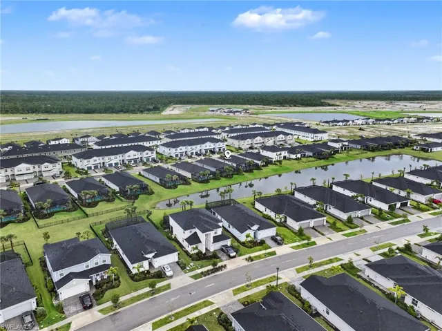 Aerial perspective of a residential community featuring dark shingle roofing, paved streets, manicured landscaping, and a central water feature