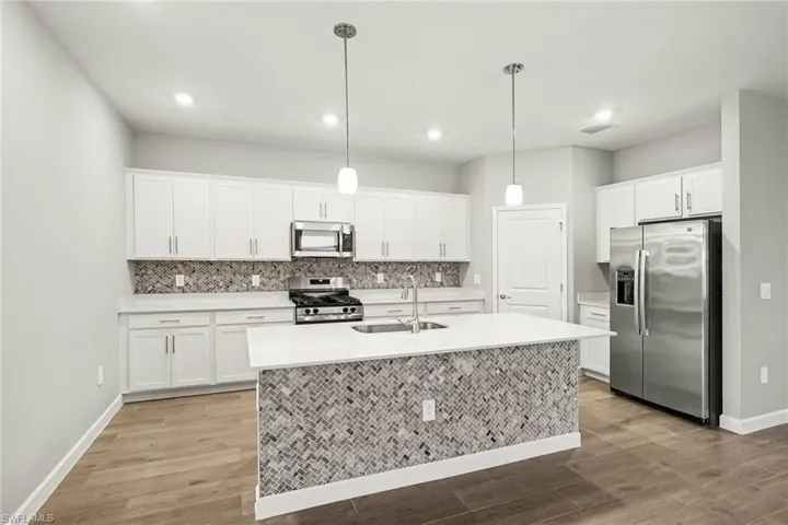 Kitchen featuring white cabinetry, quartz countertops, stainless steel appliances, herringbone-patterned tile backsplash, and wood-finish flooring