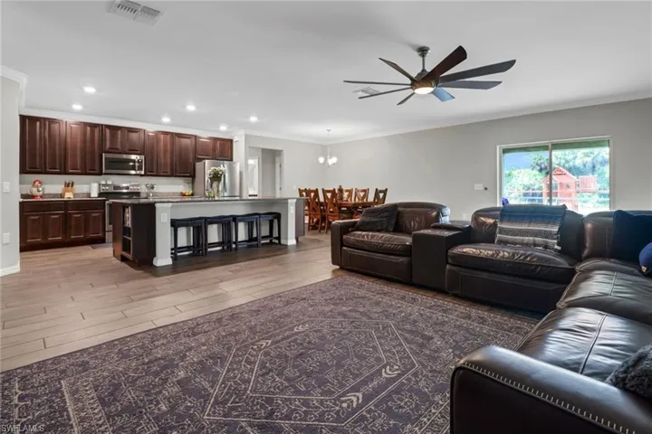 Living room featuring ceiling fan with notable chandelier, crown molding, and light hardwood / wood-style flooring