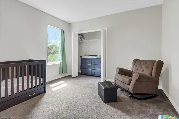 Carpeted bedroom with multiple windows, a crib, and a closet