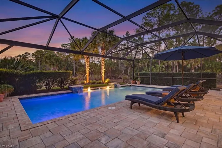 Pool at dusk featuring an outdoor pool, glass enclosure, and a patio
