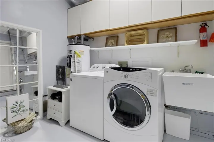 Clothes washing area featuring independent washer and dryer, cabinets, sink, and water heater
