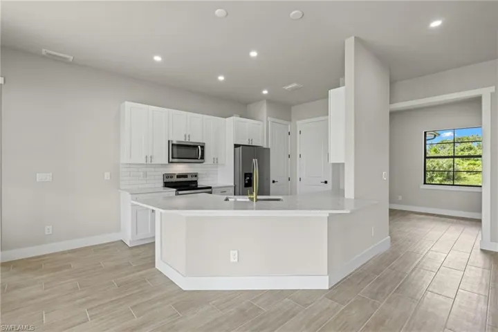 Kitchen with stainless steel appliances, sink, kitchen peninsula, backsplash, and white cabinetry