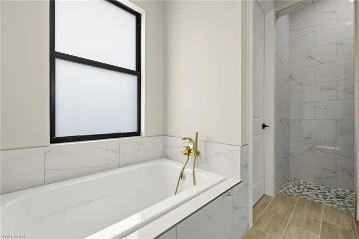 Bathroom featuring tile patterned flooring, tiled bath, and a healthy amount of sunlight