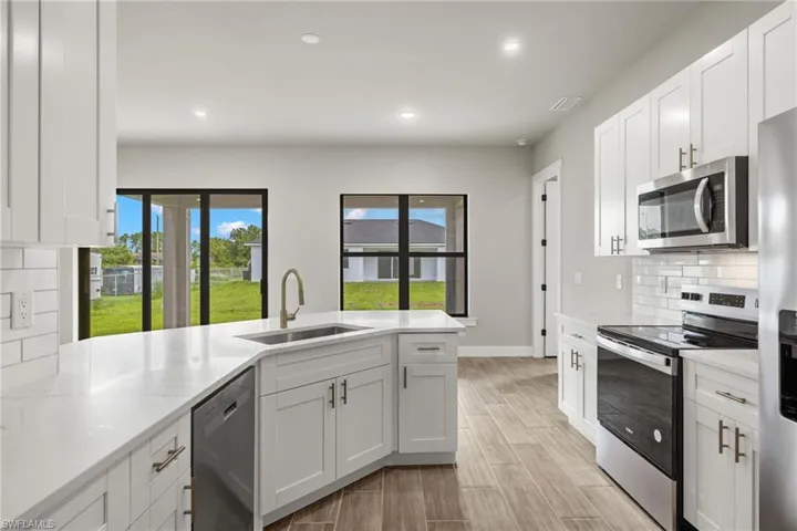 Kitchen featuring white cabinets, backsplash, light stone counters, stainless steel appliances, and sink