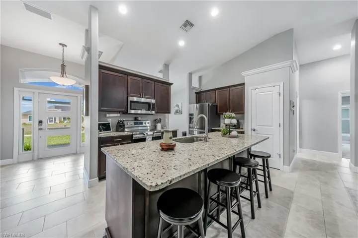 Kitchen featuring stainless steel appliances, a sink, a breakfast bar, dark brown cabinets, and a center island with sink