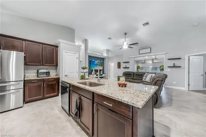 Kitchen with appliances with stainless steel finishes, a sink, a ceiling fan, light stone countertops, and open floor plan