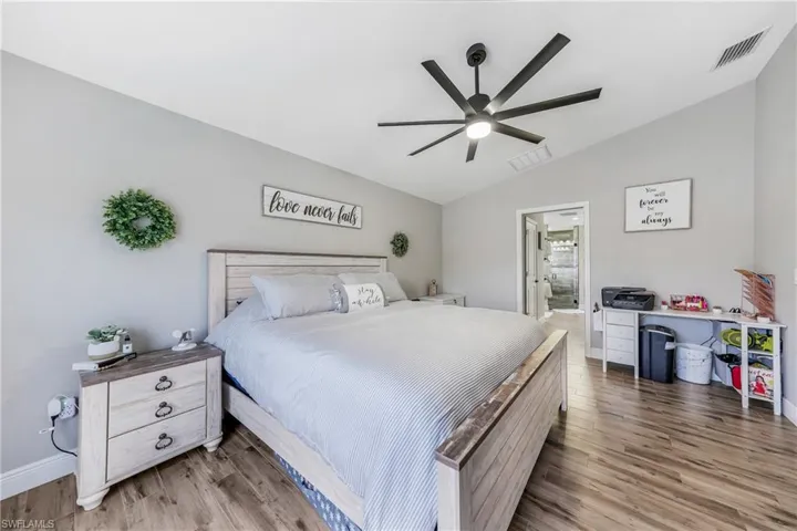 Bedroom featuring lofted ceiling, light wood-type flooring, baseboards, a ceiling fan, and ensuite bath
