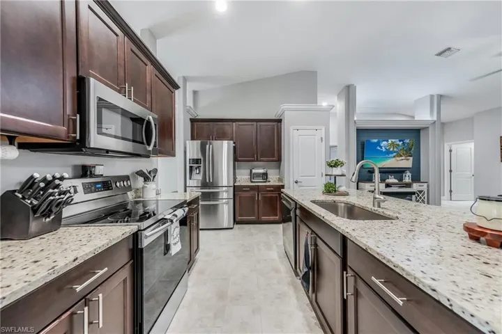 Kitchen with appliances with stainless steel finishes, a sink, light stone countertops, dark brown cabinetry, and light tile patterned floors