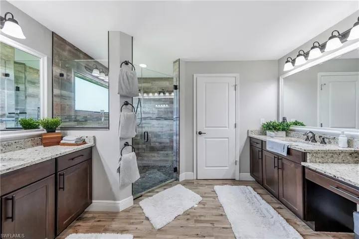 Bathroom featuring a stall shower, wood finished floors, two vanities, and baseboards