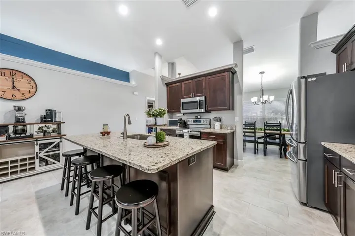 Kitchen featuring stainless steel appliances, a sink, a kitchen bar, dark brown cabinetry, and light stone countertops