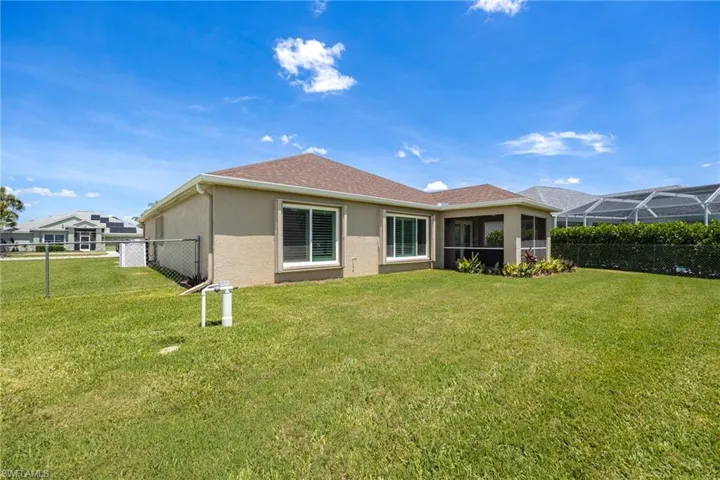 Expansive backyard featuring a screened patio, stucco exterior, multiple windows, chain link fencing, and a manicured lawn