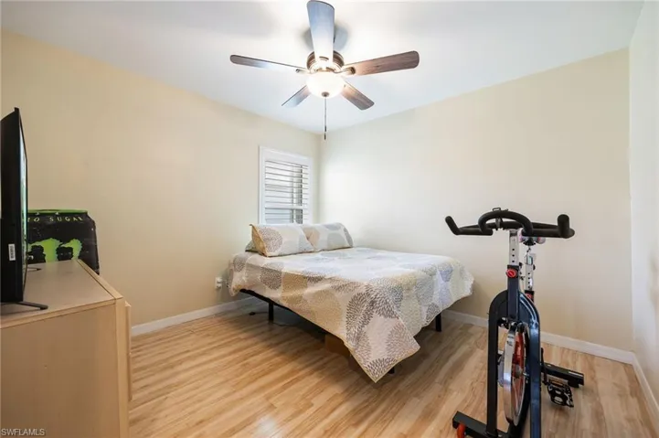 Bedroom featuring wood-finish flooring, a ceiling fan with integrated lighting, and a window with white louvered blinds