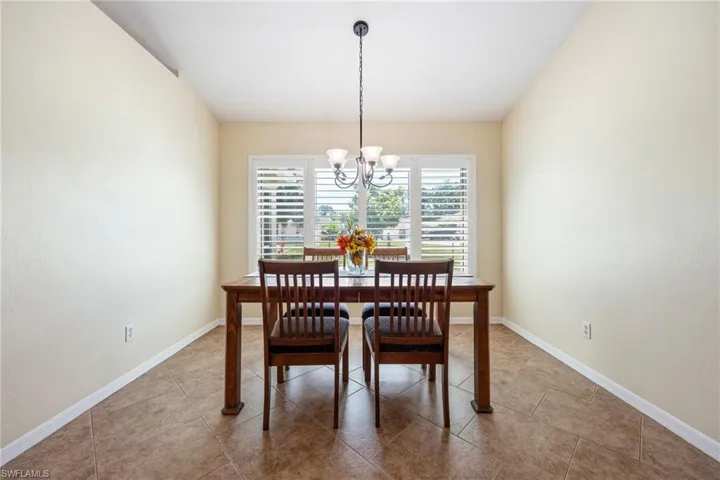 Formal dining area featuring ceramic tile flooring, neutral wall tones, a contemporary chandelier, and window shutters