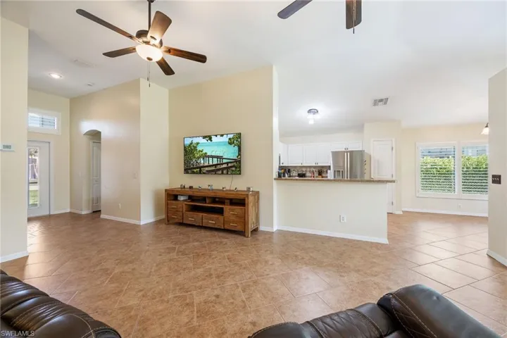 Spacious living area featuring large format tile flooring, ceiling fan with integrated lighting, an arched doorway, and built-in cabinetry