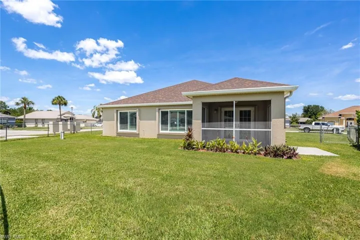 Rear exterior featuring a screened lanai, concrete patio, and a spacious lawn