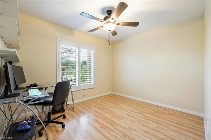 Room featuring wood-finish flooring, a window with plantation shutters, and a ceiling fan with integrated lighting