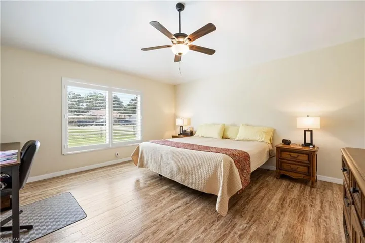 Bright interior space featuring wood-finish flooring, a ceiling fan with integrated lighting, and a large window with white plantation shutters