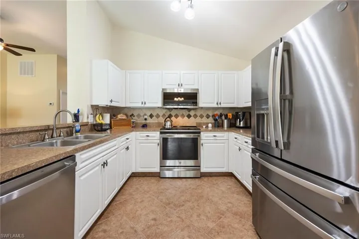 kitchen has white cabinetry, all new  stainless steel appliances, stone backsplash, and a SS double basin sink